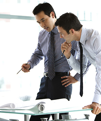 two businessman standing over and studying some forms